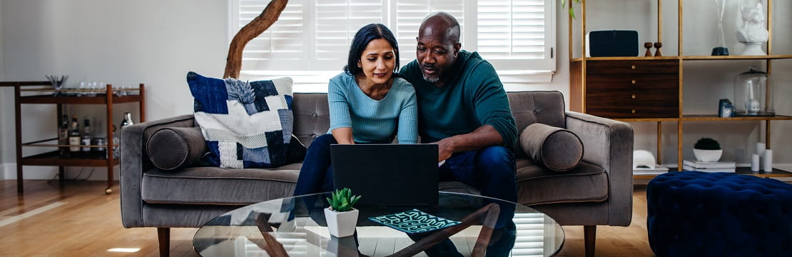 Senior couple smiles at each other while drinking out of coffee mugs. 